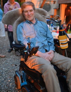Bruce smiling in his motorized wheelchair while attending an outdoor event